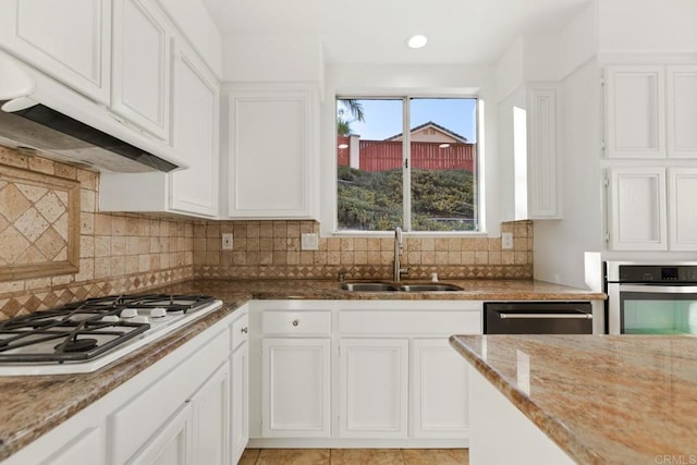 kitchen with a sink, stainless steel appliances, white cabinets, backsplash, and under cabinet range hood