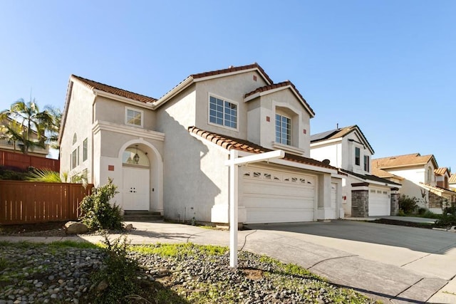 mediterranean / spanish house featuring a tiled roof, fence, driveway, and stucco siding
