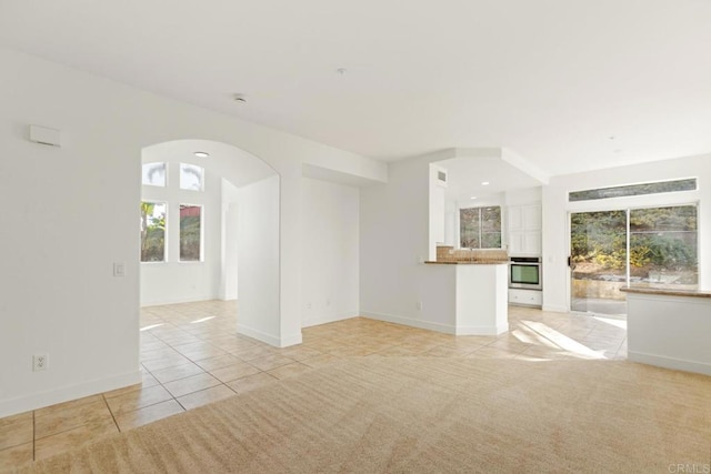 unfurnished living room featuring baseboards, arched walkways, and light tile patterned floors