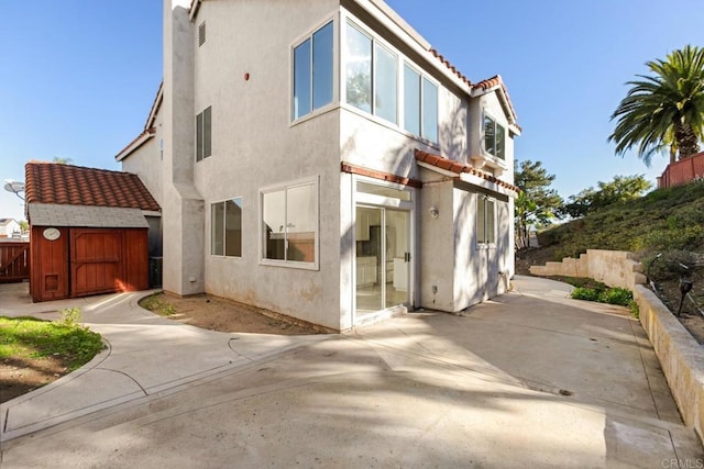 back of house with a patio area, a storage shed, fence, stucco siding, and an outbuilding