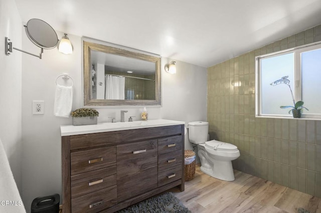 bathroom with tile walls, hardwood / wood-style flooring, vanity, toilet, and a shower with curtain