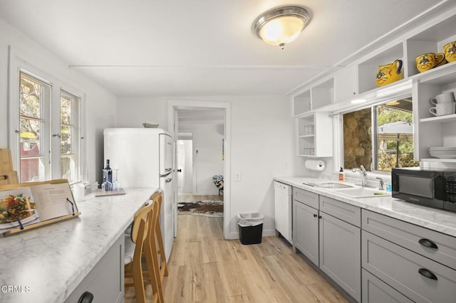 kitchen featuring gray cabinets, sink, light stone counters, light hardwood / wood-style floors, and white appliances