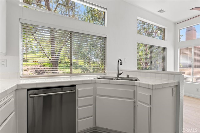 6 Daytona Dr Unit 128, Laguna Niguel, CA 92677 - kitchen featuring stainless steel dishwasher, tile counters, plenty of natural light, and white cabinetry