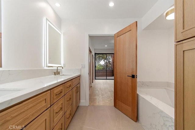 bathroom with double vanity, a garden tub, recessed lighting, and a sink