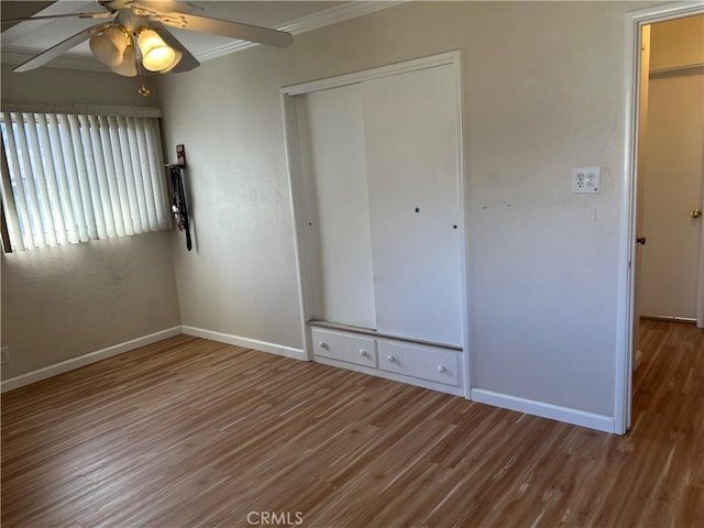 unfurnished bedroom featuring crown molding, wood finished floors, a closet, and baseboards