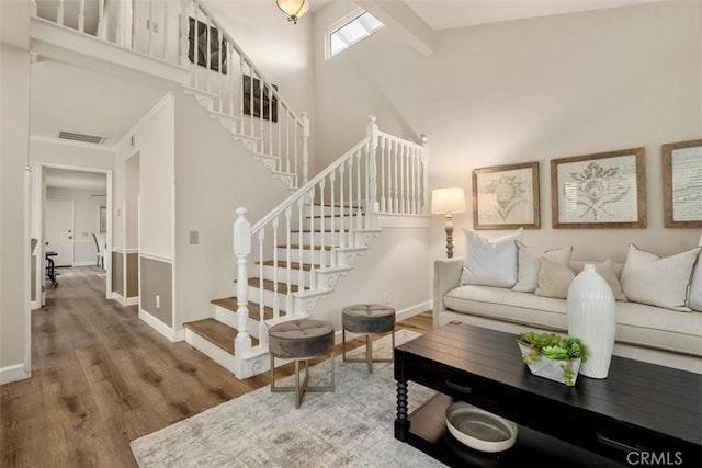 living area with visible vents, wood finished floors, baseboards, a high ceiling, and stairway