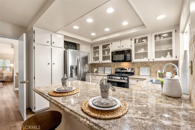 kitchen with a peninsula, recessed lighting, light stone counters, a sink, and appliances with stainless steel finishes