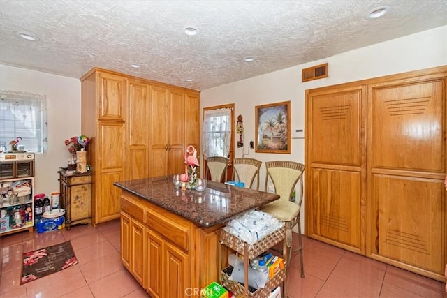 kitchen featuring a kitchen island, light tile patterned floors, a textured ceiling, and dark stone counters