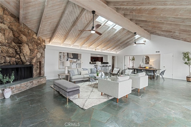 unfurnished living room with ceiling fan, a skylight, a stone fireplace, wooden ceiling, and beamed ceiling