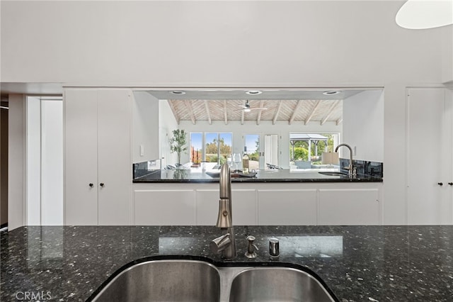 kitchen with beamed ceiling, dark stone counters, sink, and white cabinets