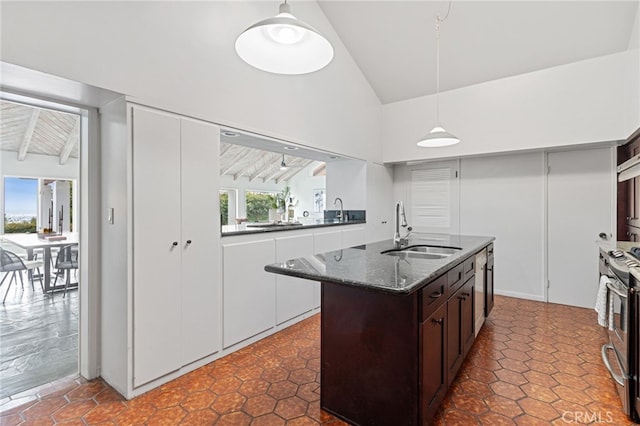 kitchen featuring pendant lighting, sink, dark stone countertops, a center island with sink, and electric stove
