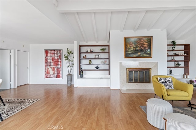 living room featuring hardwood / wood-style flooring, a high end fireplace, built in shelves, and vaulted ceiling with beams