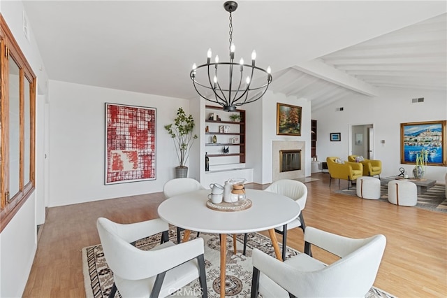dining space with vaulted ceiling with beams, a notable chandelier, and light hardwood / wood-style flooring