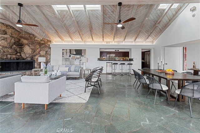 living room with beamed ceiling, a stone fireplace, wooden ceiling, and a skylight