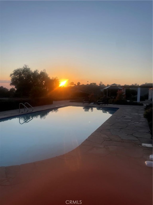 pool at dusk featuring a patio