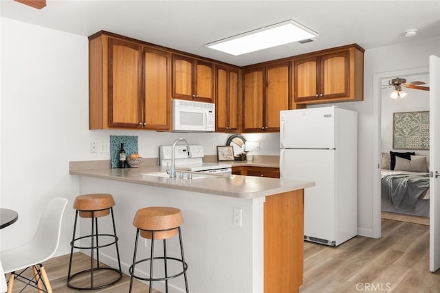 kitchen with white appliances, ceiling fan, a kitchen breakfast bar, light hardwood / wood-style floors, and kitchen peninsula