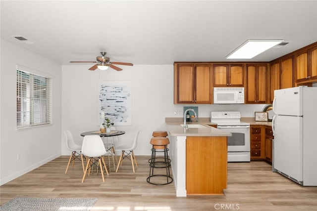 kitchen with light hardwood / wood-style floors, white appliances, kitchen peninsula, and sink