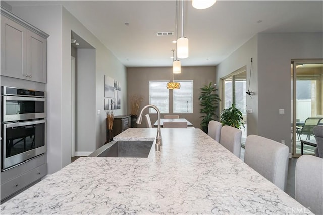 kitchen with sink, gray cabinetry, light stone counters, pendant lighting, and stainless steel double oven