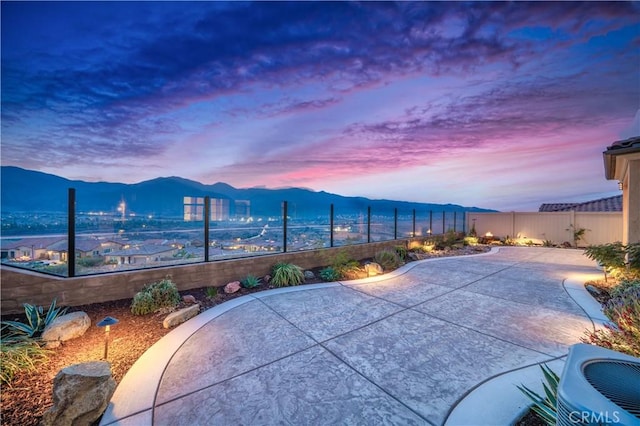 patio terrace at dusk featuring central AC, a fenced backyard, and a mountain view