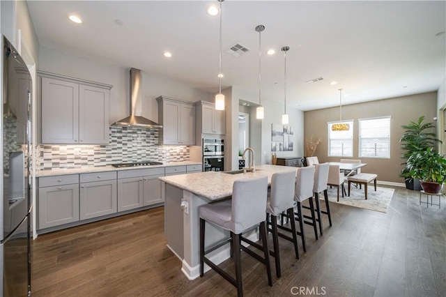 kitchen featuring pendant lighting, sink, a kitchen breakfast bar, a center island with sink, and wall chimney exhaust hood