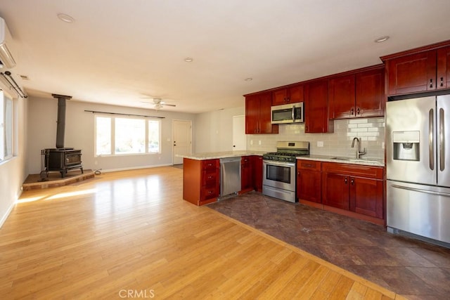 kitchen featuring sink, light wood-type flooring, a wood stove, kitchen peninsula, and stainless steel appliances