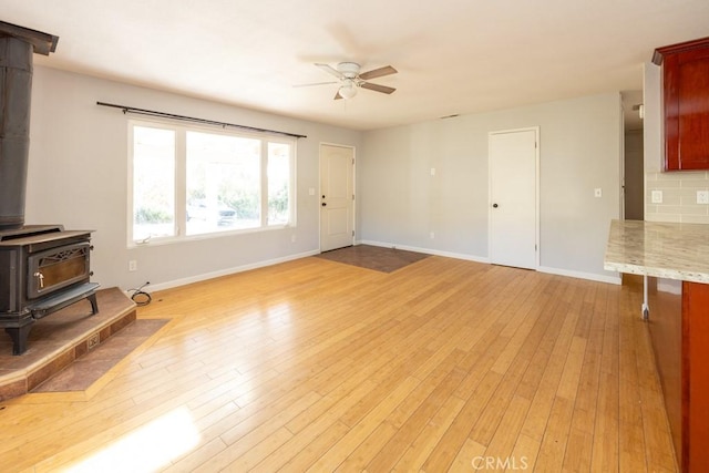 living room with ceiling fan, a wood stove, and light hardwood / wood-style floors