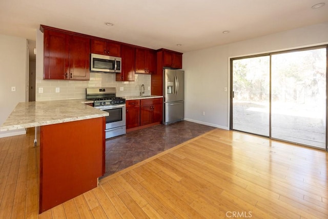 kitchen featuring sink, wood-type flooring, appliances with stainless steel finishes, kitchen peninsula, and decorative backsplash