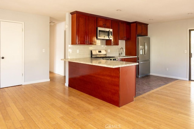 kitchen with stainless steel appliances, kitchen peninsula, light wood-type flooring, and decorative backsplash