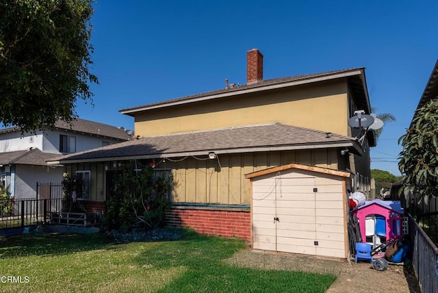 back of property featuring brick siding, an outdoor structure, fence, a yard, and a storage unit