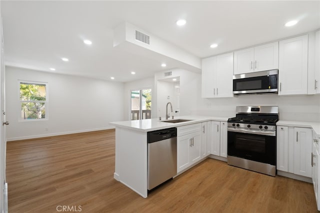 kitchen featuring light wood-style flooring, a peninsula, a sink, visible vents, and appliances with stainless steel finishes