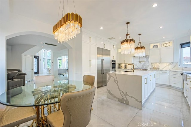 kitchen featuring white cabinetry, stainless steel appliances, decorative light fixtures, and an island with sink