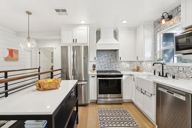 kitchen featuring stainless steel appliances, premium range hood, white cabinetry, and light hardwood / wood-style flooring