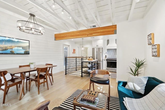 living room featuring light wood-type flooring, an inviting chandelier, track lighting, and beam ceiling