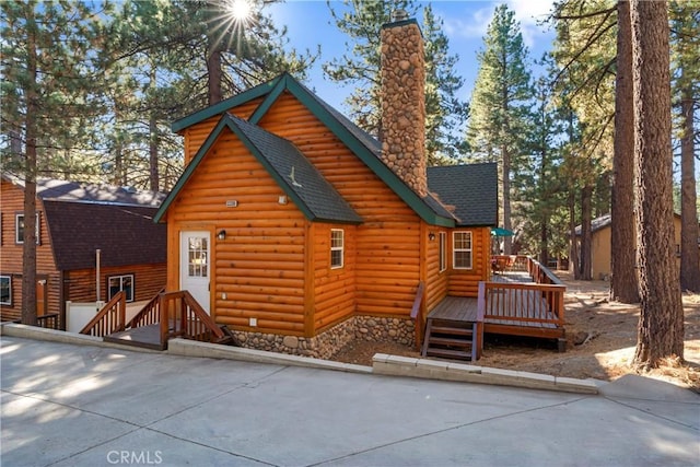 exterior space with a deck, log veneer siding, roof with shingles, and a chimney