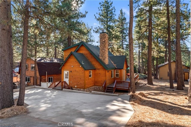 view of front of home with faux log siding, a chimney, a deck, and roof with shingles