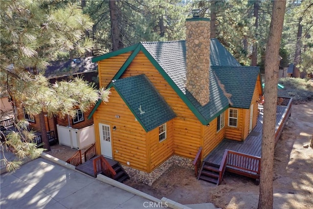 view of front of house with log veneer siding, roof with shingles, a chimney, and a wooden deck