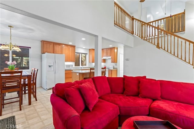 living area with a towering ceiling, stairway, an inviting chandelier, light floors, and recessed lighting