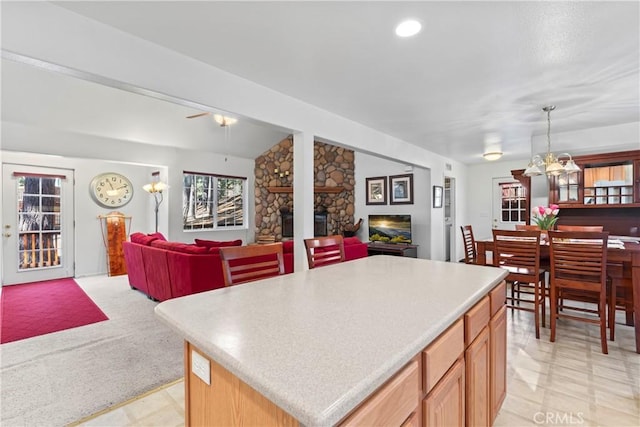 kitchen featuring light countertops, hanging light fixtures, open floor plan, a kitchen island, and a stone fireplace