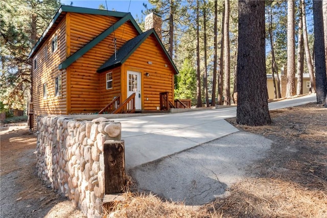 view of side of home featuring faux log siding, roof with shingles, and a chimney