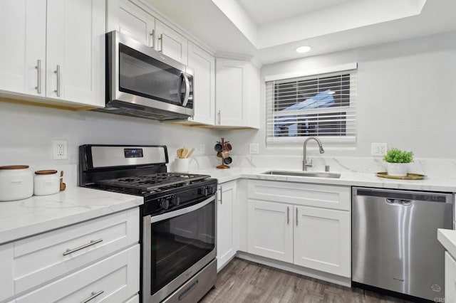 kitchen with dark wood-type flooring, light stone countertops, stainless steel appliances, white cabinetry, and a sink