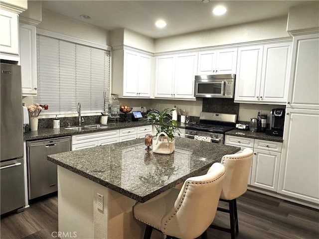 kitchen featuring appliances with stainless steel finishes, sink, white cabinets, dark hardwood / wood-style flooring, and a center island