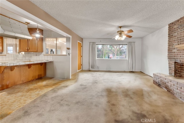 unfurnished living room with light carpet, ceiling fan, and a textured ceiling