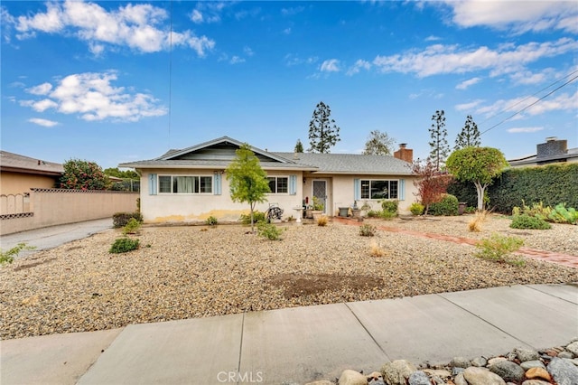 single story home featuring roof mounted solar panels, fence, and a chimney