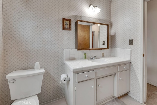 bathroom with toilet, wallpapered walls, tile patterned flooring, and vanity