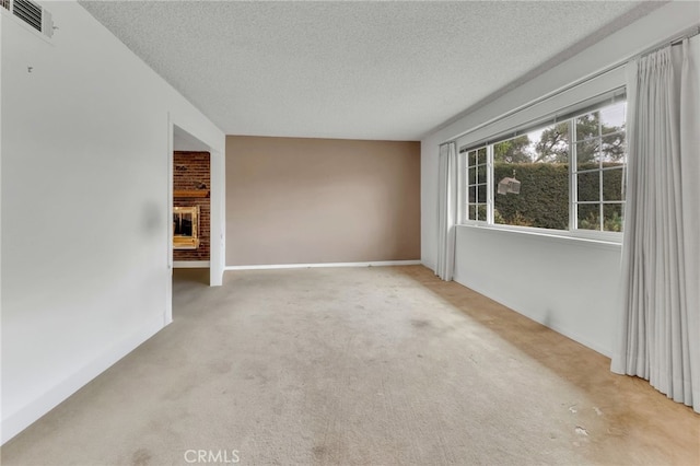 carpeted spare room with visible vents, a fireplace, a textured ceiling, and baseboards