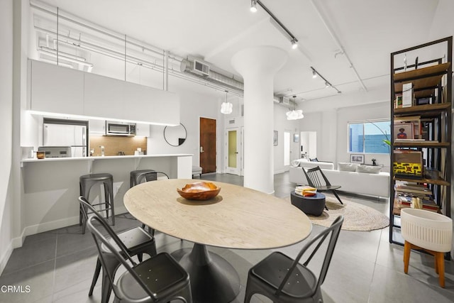 dining area with a towering ceiling, rail lighting, and light tile patterned floors