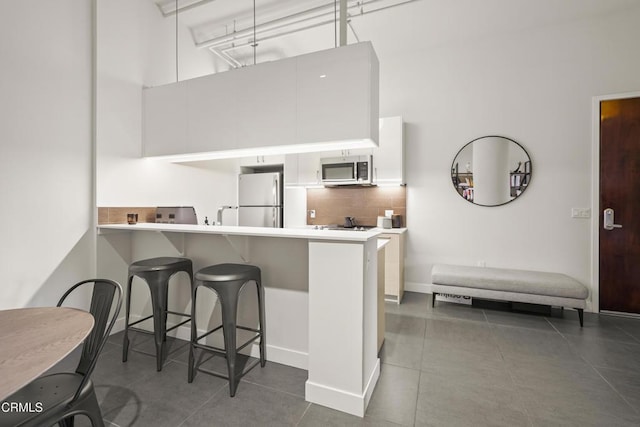 kitchen featuring white cabinetry, a kitchen breakfast bar, kitchen peninsula, stainless steel appliances, and decorative backsplash