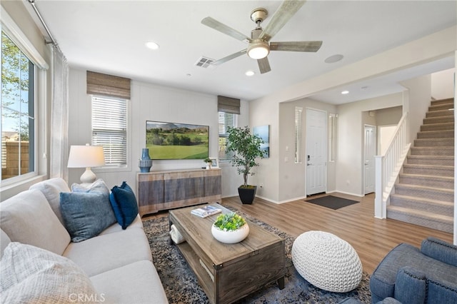 living room with a wealth of natural light, wood finished floors, visible vents, and stairs