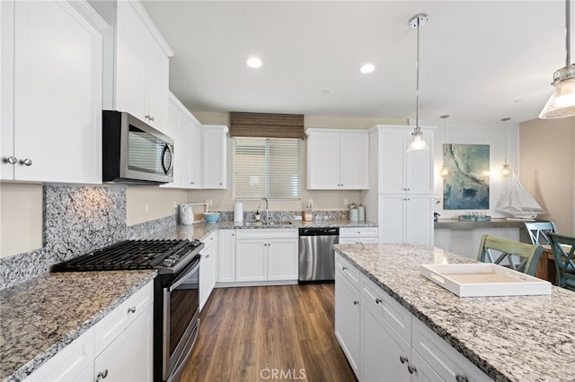 kitchen featuring stainless steel appliances, light stone counters, white cabinets, and pendant lighting