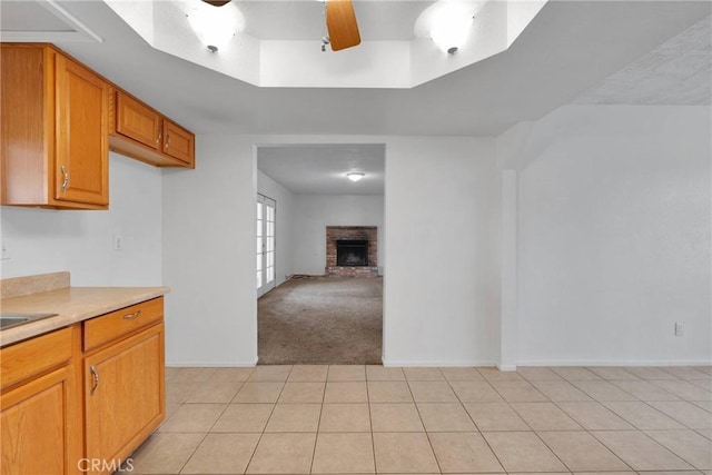 kitchen featuring a brick fireplace, light colored carpet, ceiling fan, and a tray ceiling